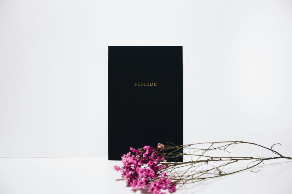 Cuaderno negro con la palabra “suicidio” y flores rosas, como símbolo de concienciación y reflexión sobre los mitos del suicidio.