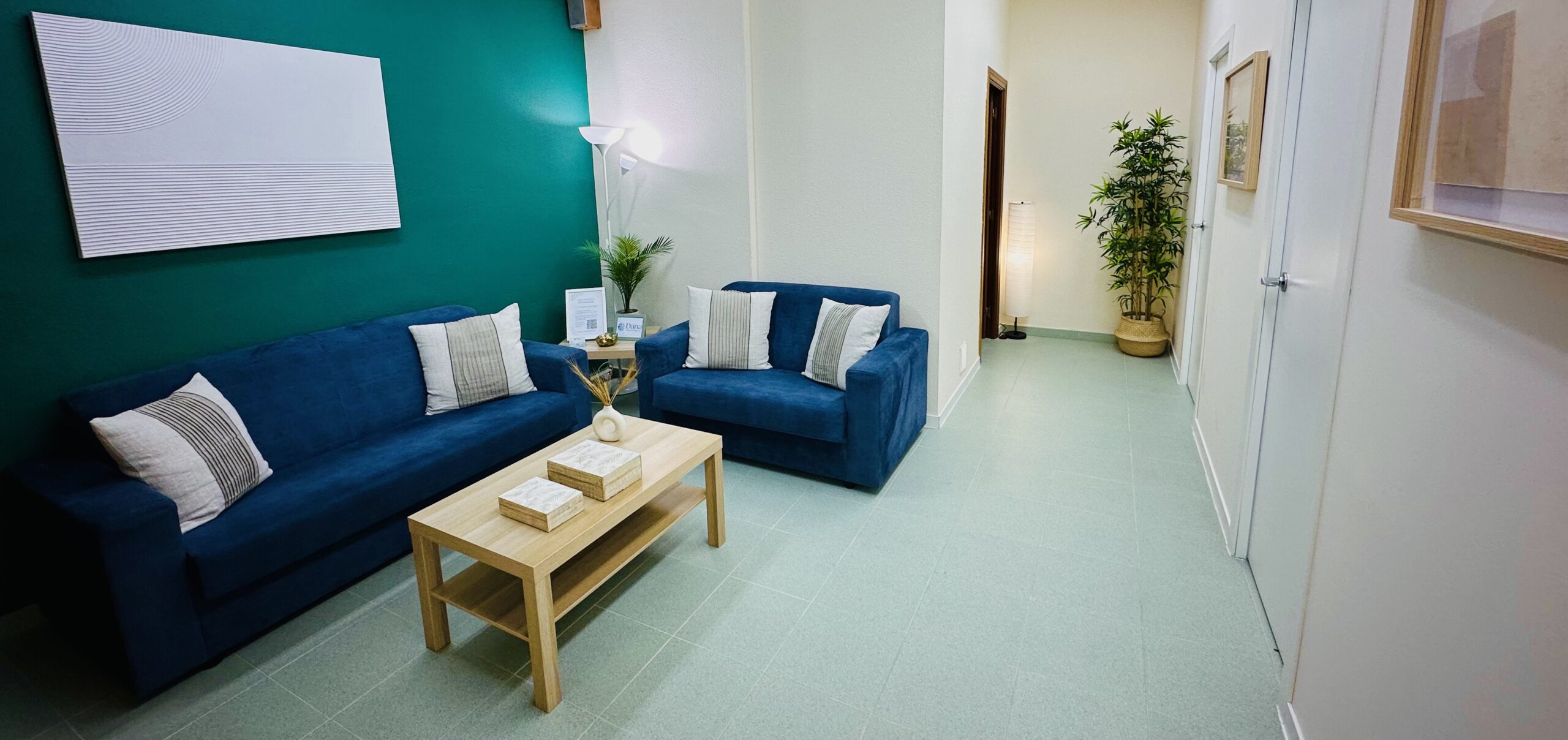 Zona de espera luminosa en Dana Psicología Getafe 30, con sofás azules, mesa de roble y plantas naturales.