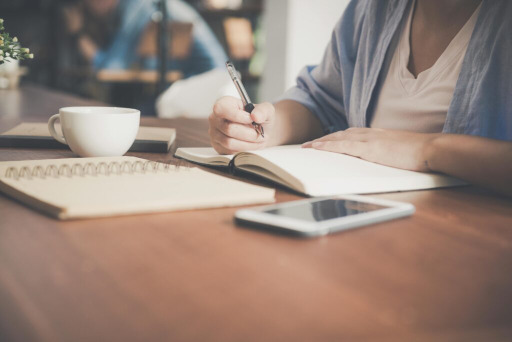 Persona escribiendo en una libreta junto a un móvil y un café, imagen sobre terapia online e inteligencia artificial en psicología.