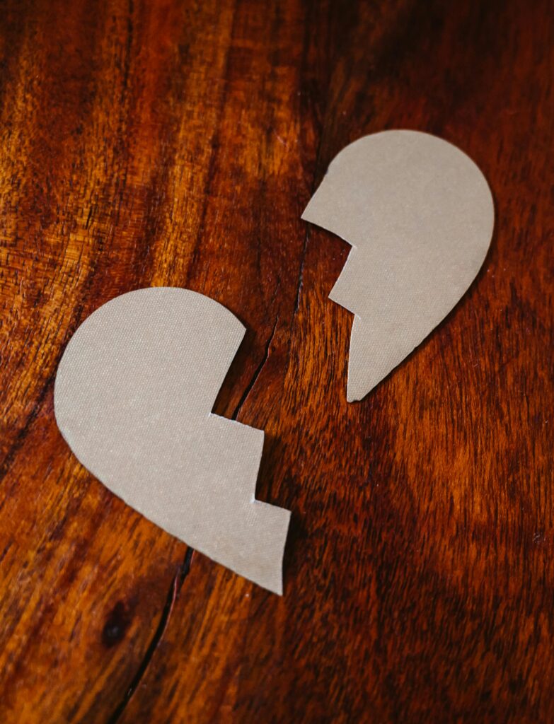 Corazón roto de papel sobre madera, símbolo de ruptura de pareja y desgaste emocional por conflictos repetidos.