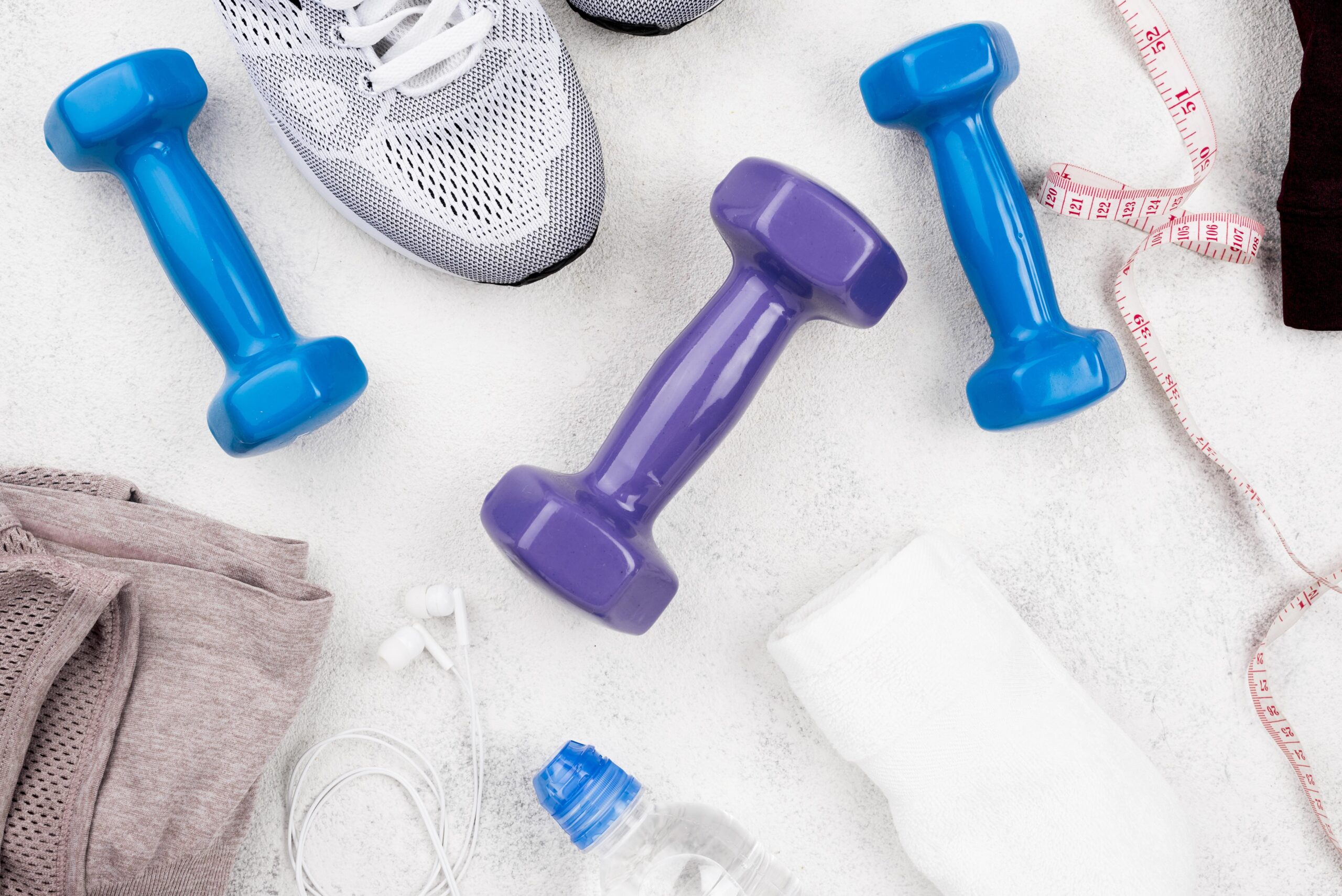 Mancuernas, cinta métrica y zapatilla deportiva, símbolo de cultura fitness, control corporal y presión estética en redes sociales.