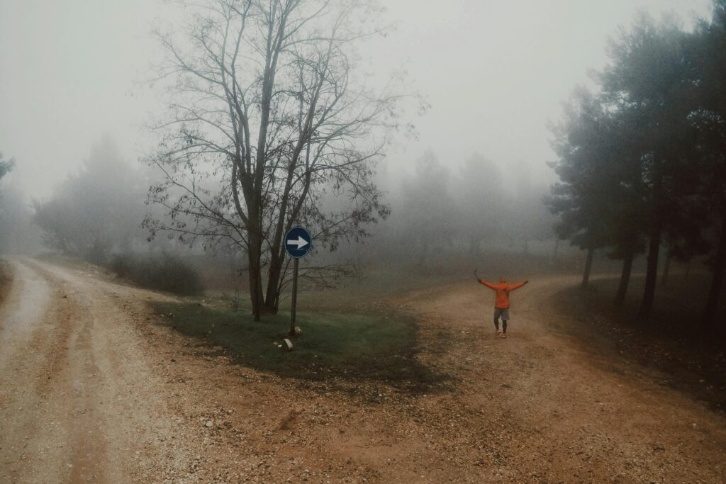 Camino que se divide entre niebla con una persona al fondo, metáfora de tomar decisiones sin claridad y seguir adelante pese a la incertidumbre.