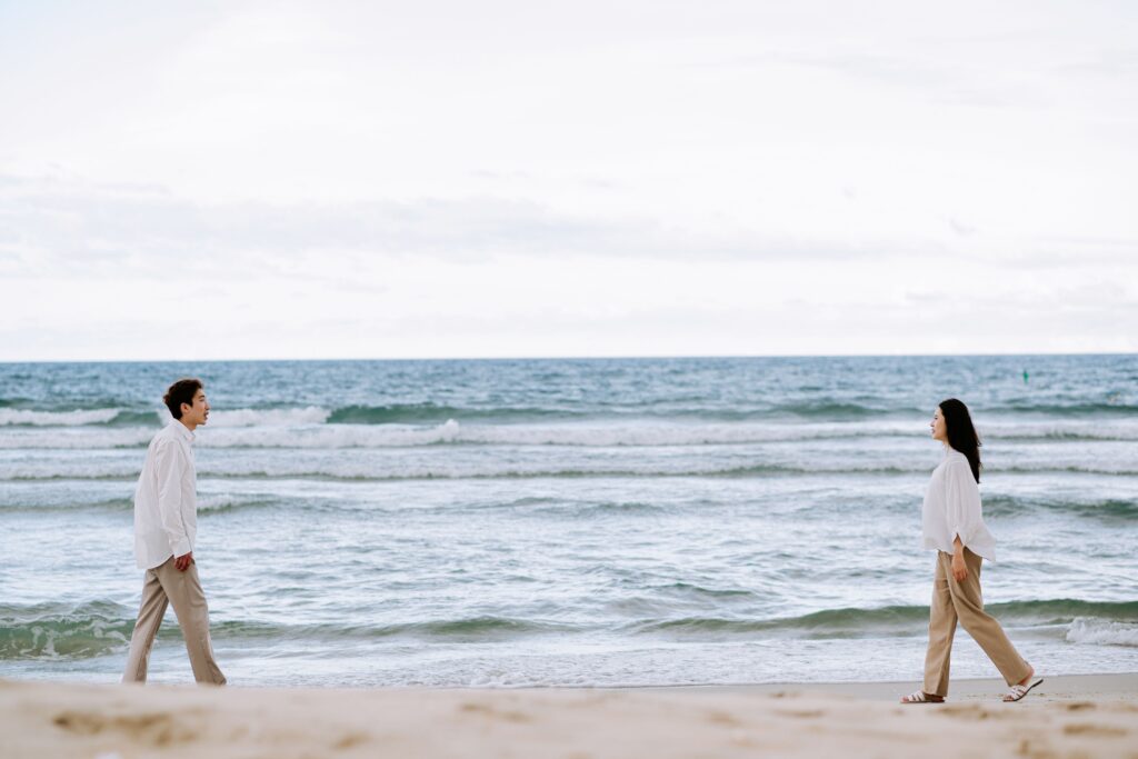 Pareja separada en la playa al atardecer, símbolo de distancia emocional, discusiones y dificultades de convivencia en verano.