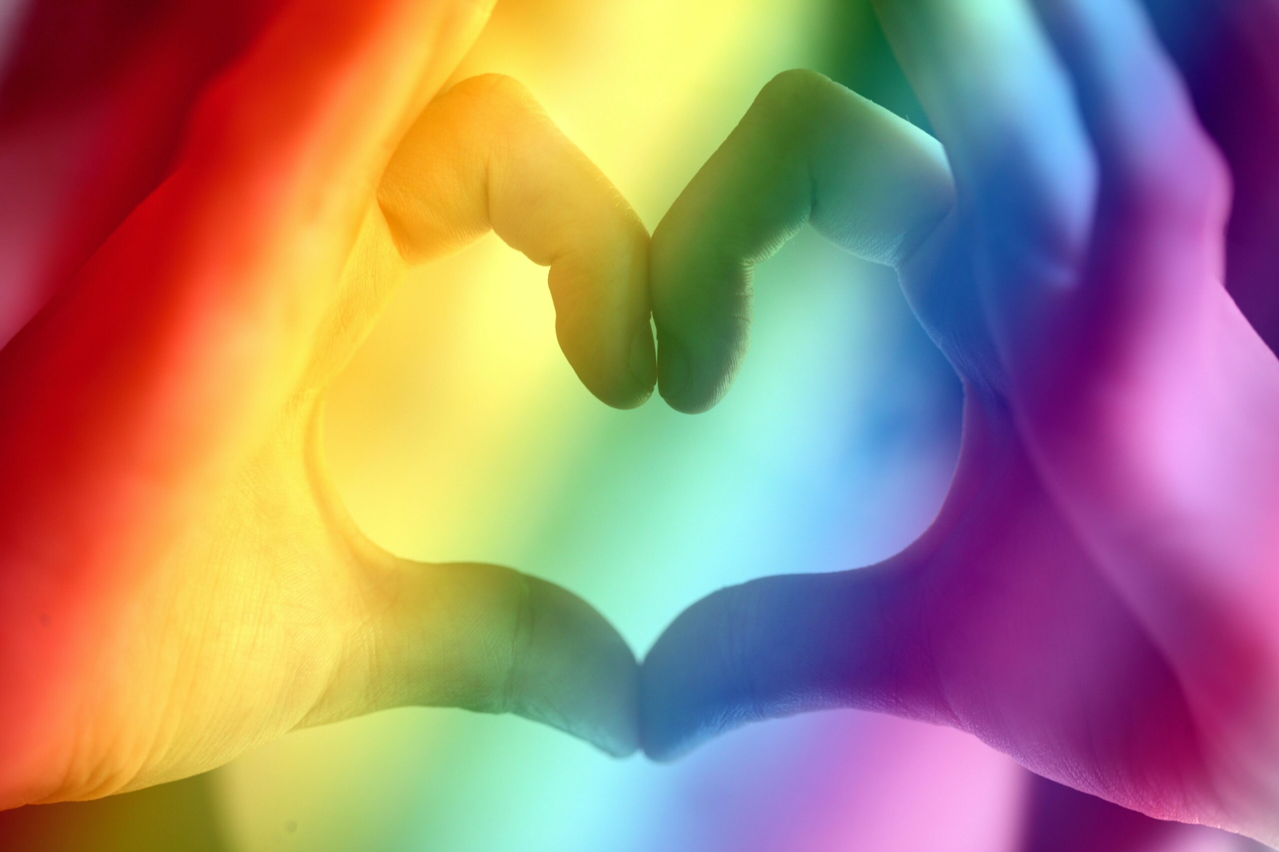 Manos formando un corazón sobre los colores del arcoíris, imagen sobre diversidad afectivo-sexual, respeto e igualdad LGTBI+.